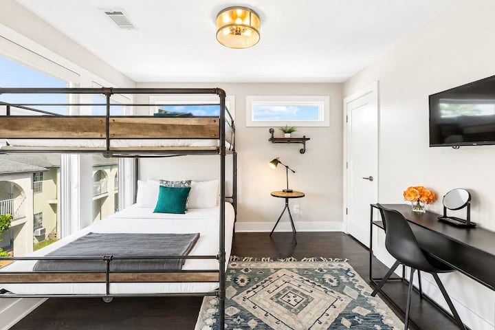 Industrial style queen over queen bunk bed, styled in cozy neutrals - Bright room with oversized windows, geometric rug, and desk setup for work or study - Thoughtful decor with greenery, light wood accents, and clean minimalist lines