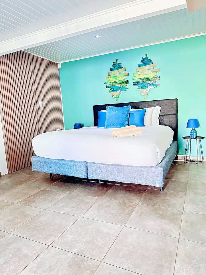 Pumzika kwa mtindo na mpangilio huu wa kitanda cha kifahari, unaovutia kwa kutuliza rangi ya maji, sanaa ya kipekee ya ukuta na mapambo ya kisasa. Mapumziko ya kukaribisha baada ya jasura zako za kisiwa.