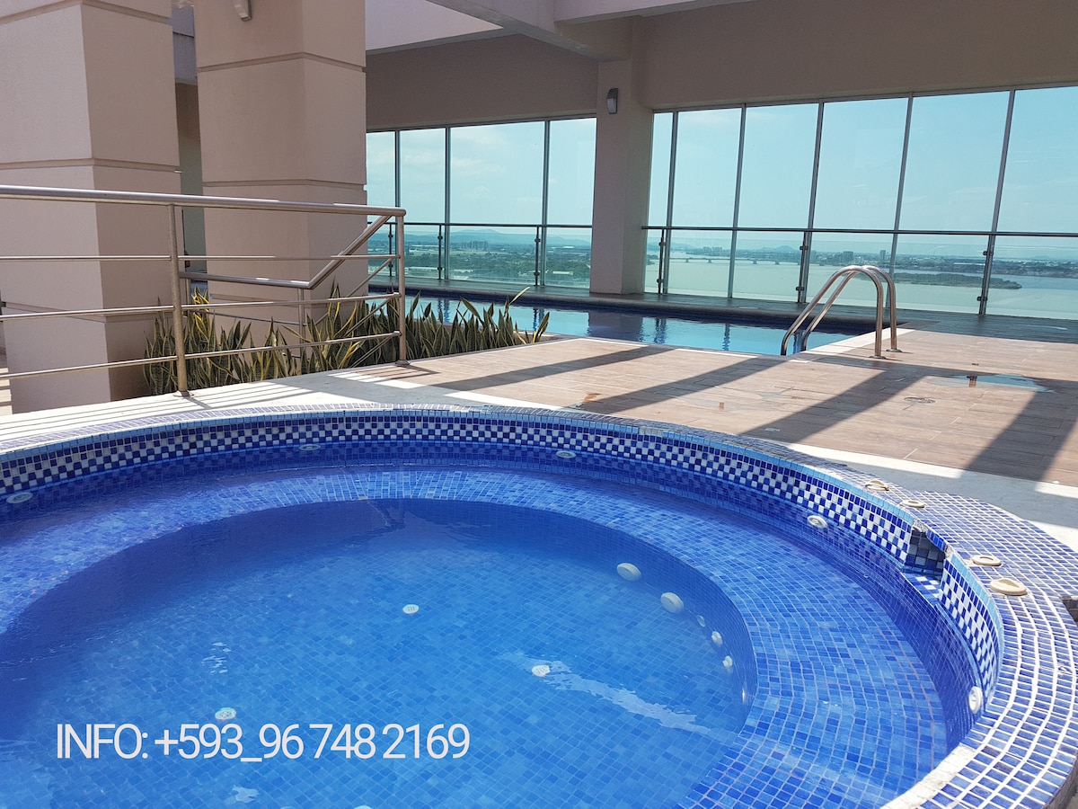 A serene terrace area features a shimmering outdoor pool with panoramic windows overlooking the river. Adjacent to the pool, a circular Jacuzzi invites relaxation, surrounded by elegant tiles and carefully arranged greenery. The space is flooded with natural light for a refreshing ambiance.