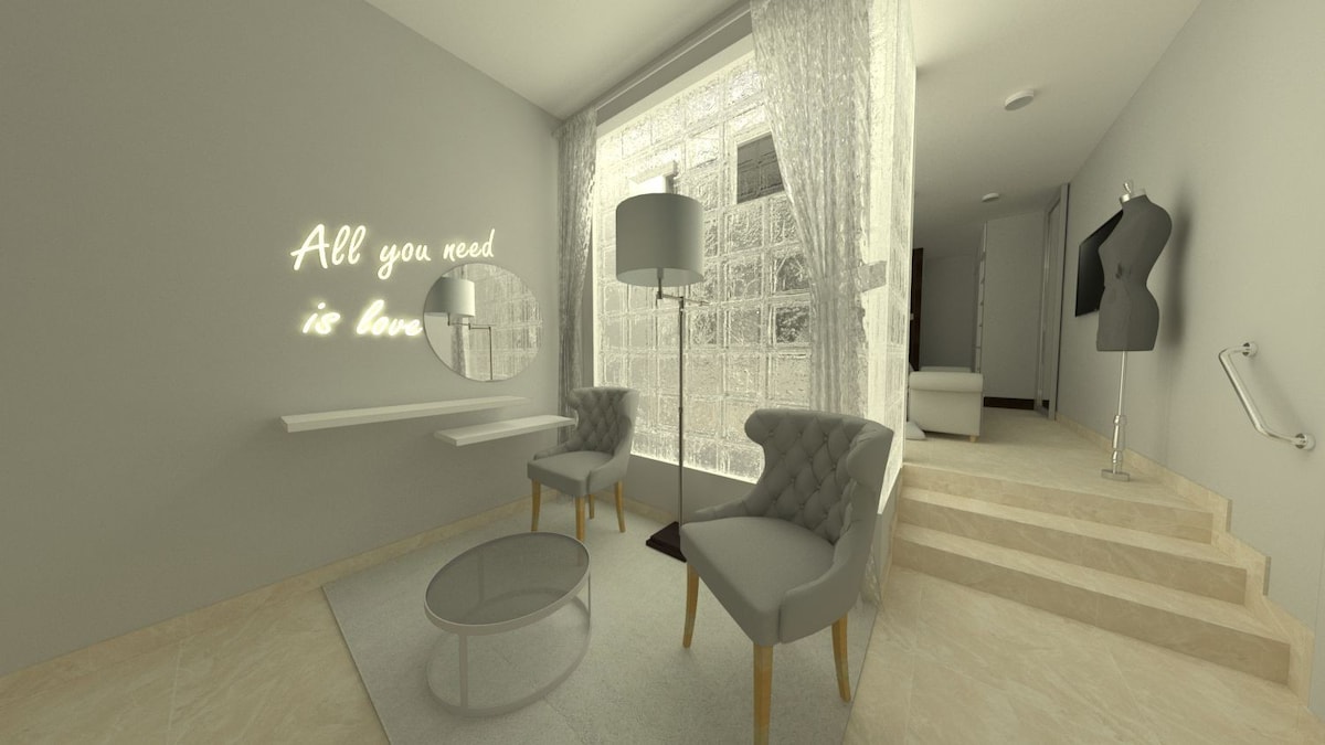 A stylish sitting area is illustrated with two plush gray armchairs next to a circular glass coffee table. A modern floor lamp stands nearby, and large windows allow natural light to fill the space. A minimalist mirror and decorative art are present on the light gray walls.