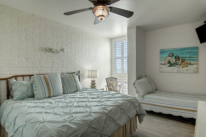 Unwind in your coastal-inspired bedroom featuring comfy beds, beach artwork, and a gentle ceiling fan for peaceful nights.
