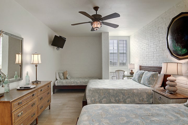 Unwind in your coastal-inspired bedroom with twin beds, exposed brick walls, and a gentle ceiling fan creating the perfect oceanside atmosphere.