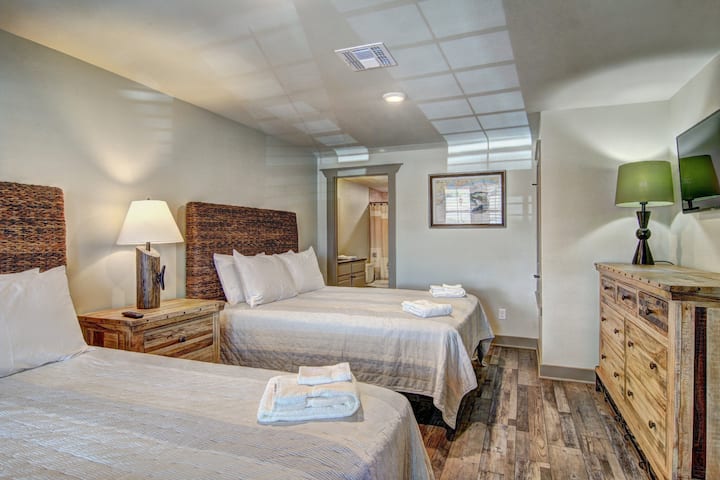 Your cozy retreat features two comfortable beds with rustic headboards, warm lighting, and thoughtful touches like fresh towels waiting for your arrival.