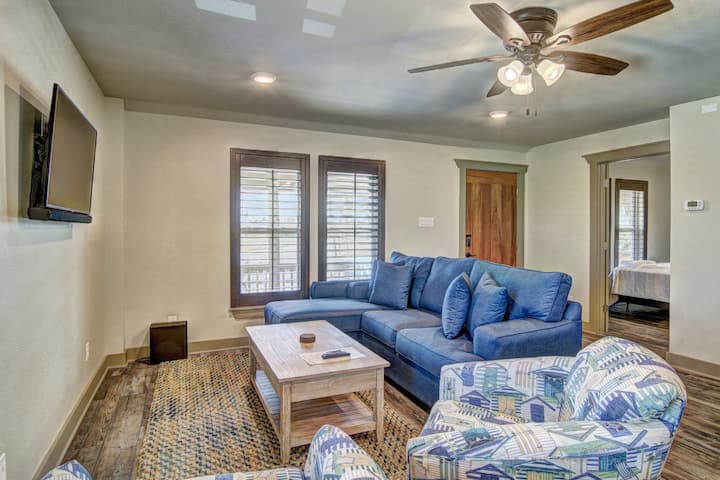 Relax in your spacious living room featuring a cozy blue sectional sofa, perfect for movie nights under the gentle breeze of the ceiling fan.