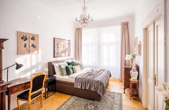 Chambre lumineuse et élégante avec un lit double confortable, un lustre et des tons neutres doux.
