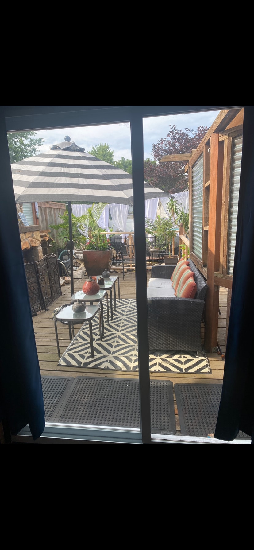 A private patio area is showcased, featuring a stylish seating arrangement with a striped umbrella above. Decorative plants are positioned throughout, enhancing the outdoor space. A patterned rug lies beneath a table set for dining, providing an inviting atmosphere for relaxation or meals.