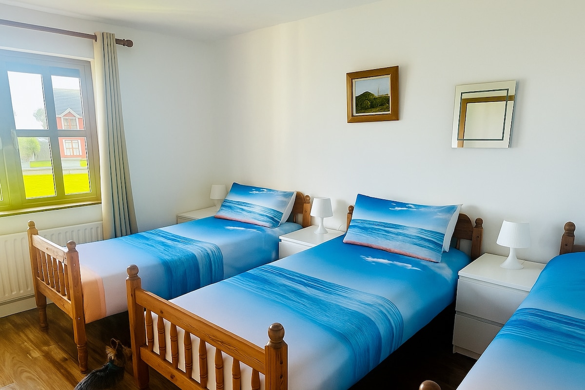 明亮宽敞的卧室，配备三张单人床和清新的海洋风格床上用品。 房间充满了大窗户的自然光线。 它有桌子和灯具、抛光的木地板和简单的海岸装饰，营造宁静、轻松的氛围。
