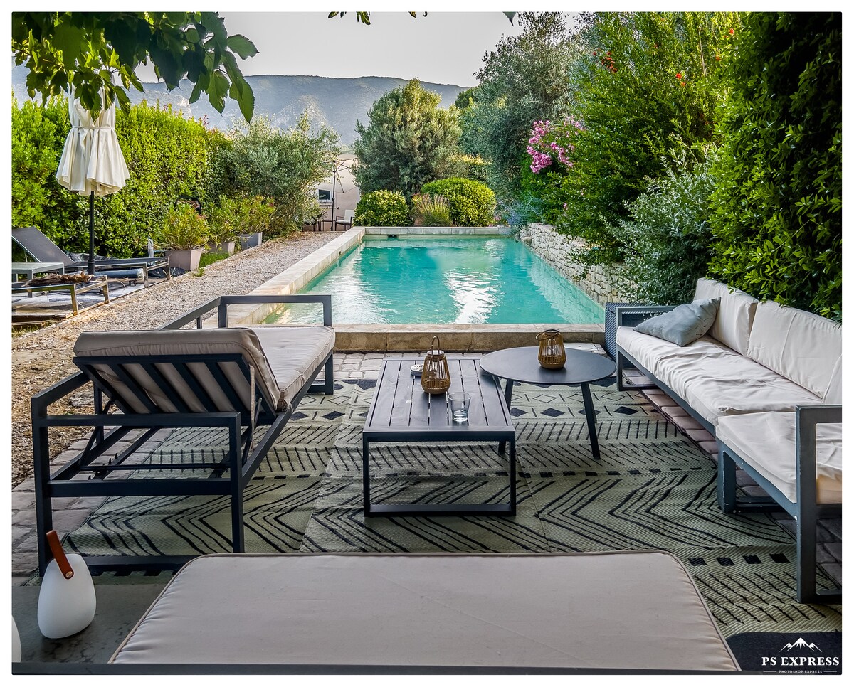 An outdoor seating area is arranged around a modest coffee table, complemented by comfortable lounge chairs. A private pool is visible in the background, accompanied by surrounding greenery, creating a peaceful and inviting environment.