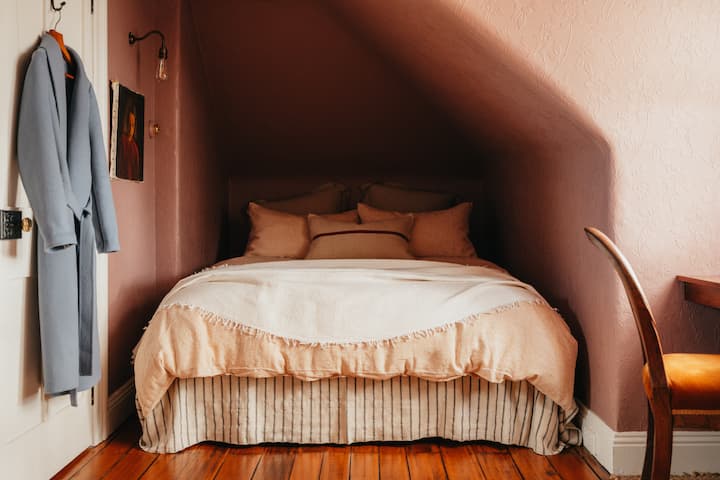 A restful queen bed beneath sloping ceilings, wrapped in custom-painted anaglypta wallpaper and soft light.