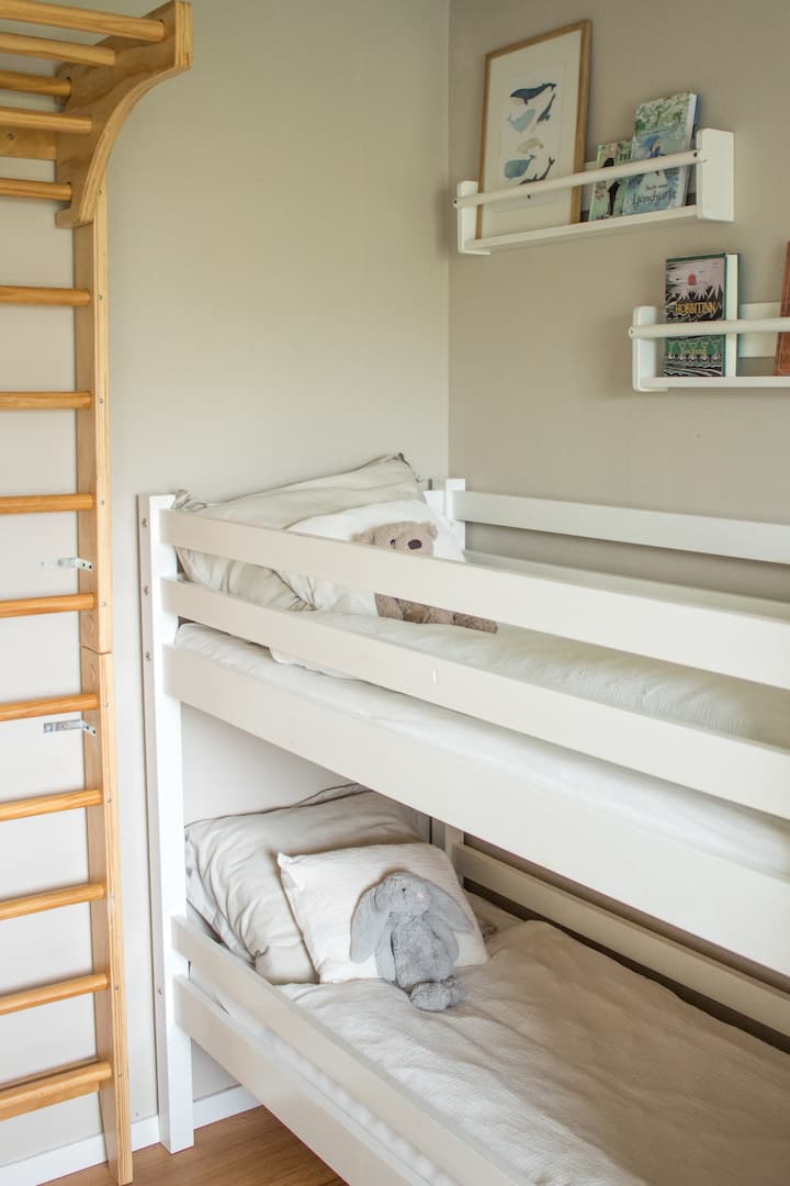 Una habitación infantil luminosa y acogedora con literas (tamaño 70x160 cm), ropa de cama suave y una selección de libros, juguetes y obras de arte.