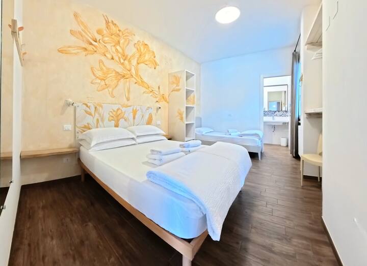 Elegantná izba s ručne zdobenou stenou v teplých zlatých odtieňoch, ktorá vytvára elegantnú a príjemnú atmosféru. Pohodlná posteľ, prirodzené svetlo z veľkých okien a ďalší priestor s jednolôžkovou posteľou. Priľahlá vlastná kúpeľňa.
