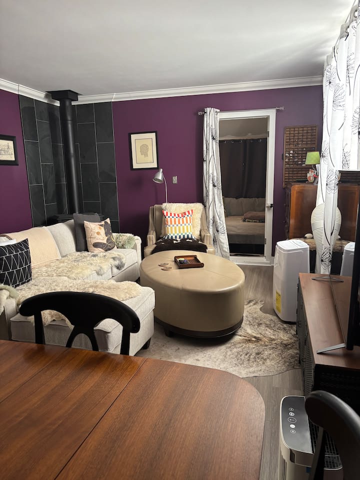 Living room with sectional sofa, armchair, dining table with chairs, fireplace, TV, AC, and an air purifier.  Looking towards front room that has a single daybed.