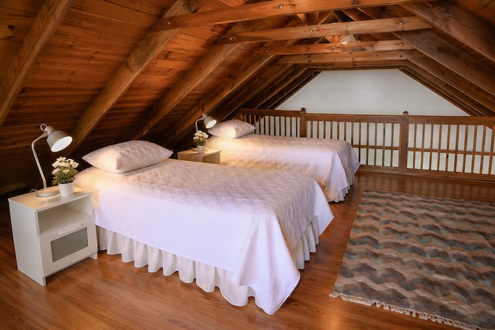 Cozy loft sleeping area with two queen beds, warm wood ceilings, and an open layout that adds character and extra space for families or groups.