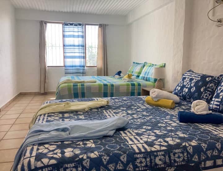 ️ ห้องพักกว้างขวางพร้อมเตียงเดี่ยว 2 เตียงและเตียงคู่ ผ้าปูที่นอนสีฟ้า โคมไฟตั้งโต๊ะ และหน้าต่างที่ให้แสงธรรมชาติเข้ามา ที่พักที่สะดวกสบายและใช้งานได้จริง เหมาะสำหรับครอบครัวหรือกลุ่ม ✨