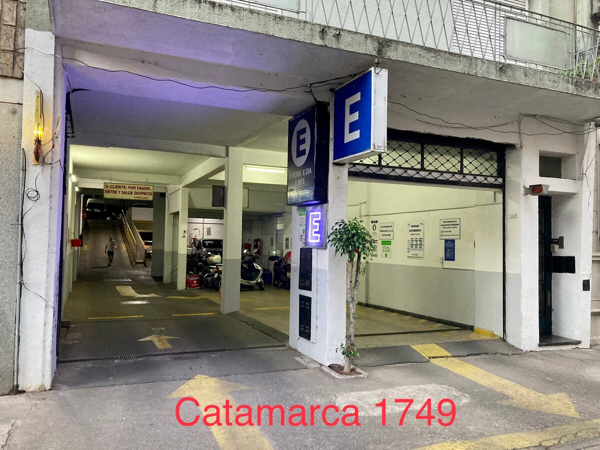 The entrance to a secure parking facility is visible, marked by a large sign. Vehicles are parked in designated spaces, with a clear pathway leading towards the exit ramp. The area is well-lit, providing a safe environment for guests.