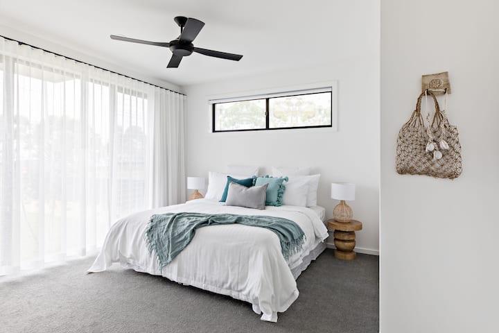 Dormitorio con cama tamaño king, muebles suaves y grandes ventanales para disfrutar de la luz y la comodidad