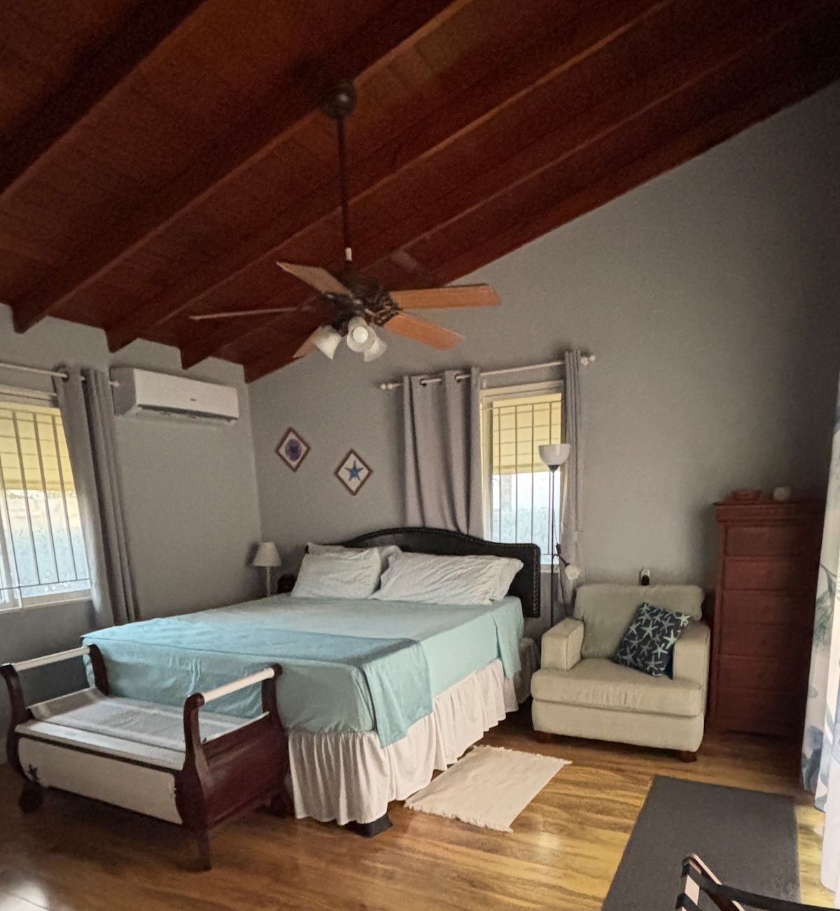 El dormitorio principal cuenta con una cama tamaño king, una silla de lectura y mucho espacio de almacenamiento (no se muestra).  Mantente fresco con el aire acondicionado mini-split y el ventilador de techo.  Disfruta de la brisa fresca del mar y de una vista directa a la terraza de la piscina.