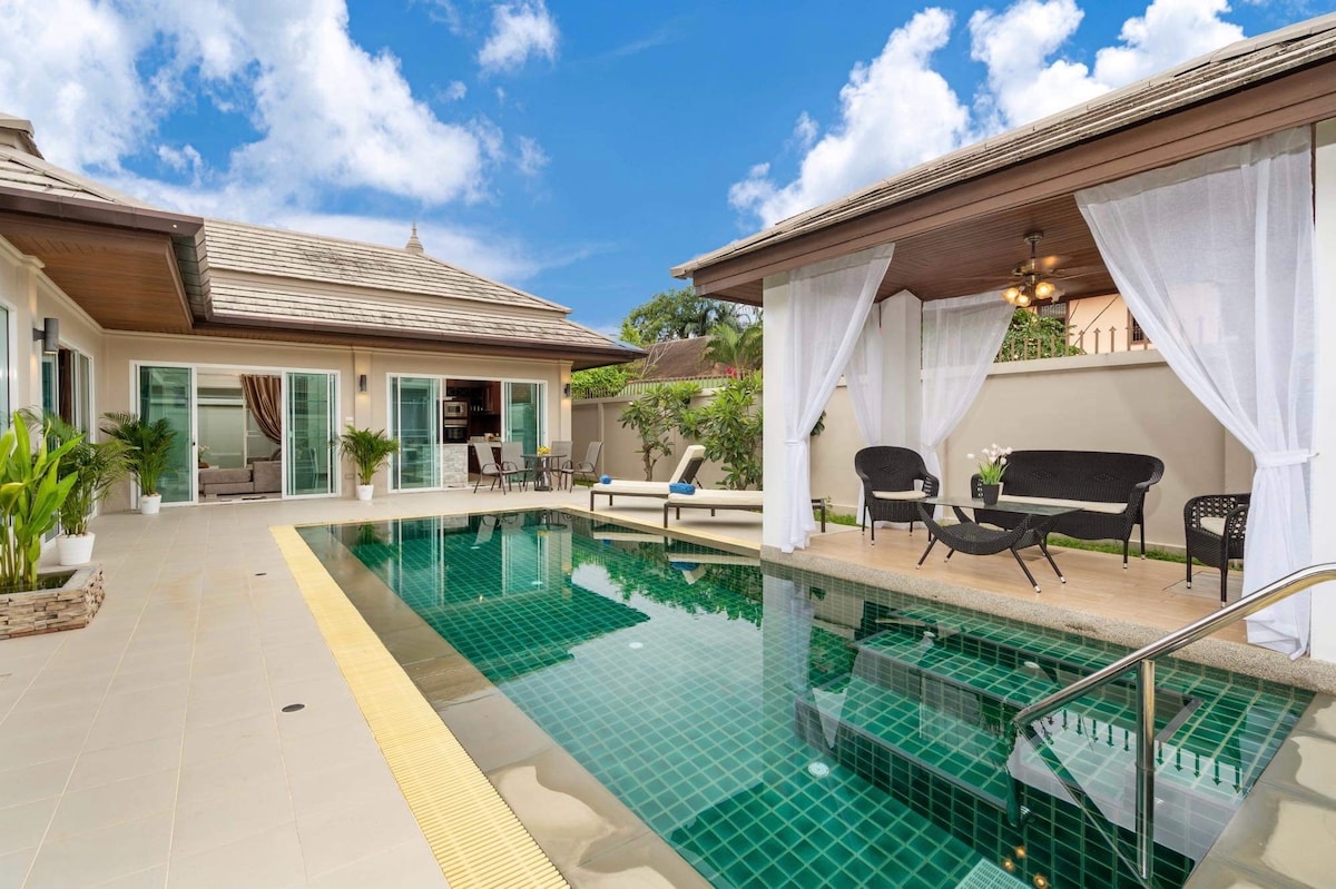 A private swimming pool is framed by a sun terrace, featuring loungers and shaded seating arrangements. The villa's exterior is highlighted with large glass doors that lead to open living spaces, connecting both relaxation and dining areas seamlessly.