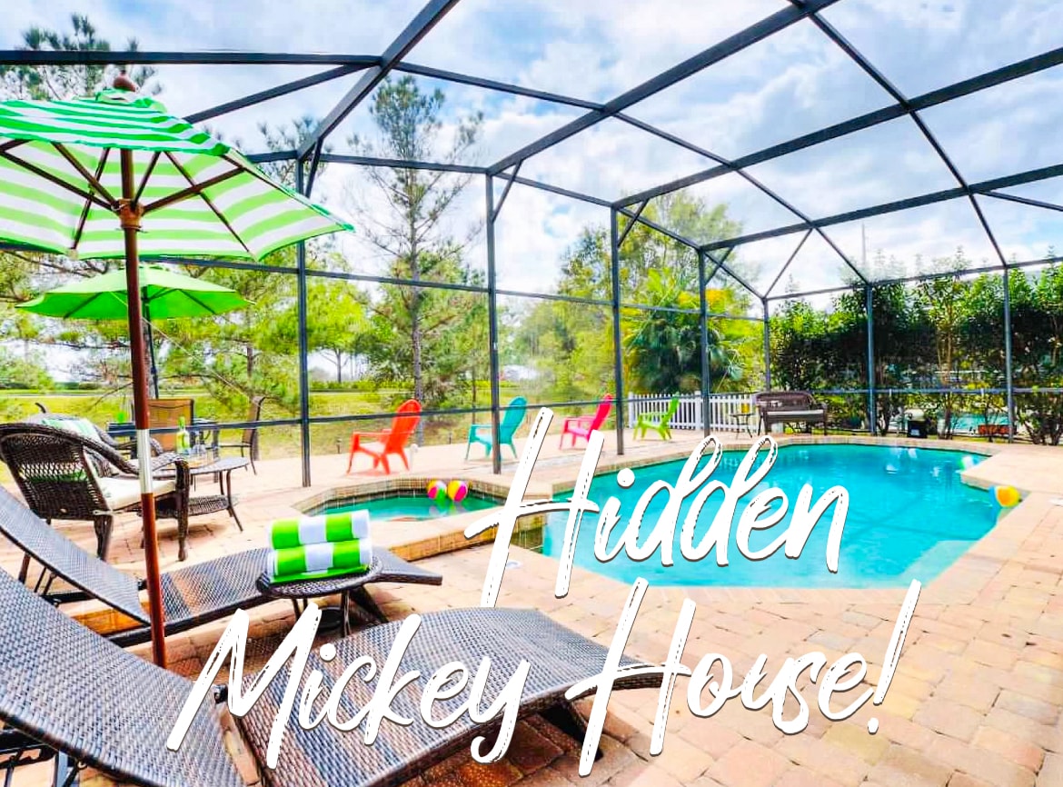 The outdoor area features a screened-in pool surrounded by several lounge chairs and colorful chairs along the perimeter. A large patio umbrella provides shade, while playful decorations can be seen floating in the pool. Lush greenery borders the space, enhancing the tranquil atmosphere.