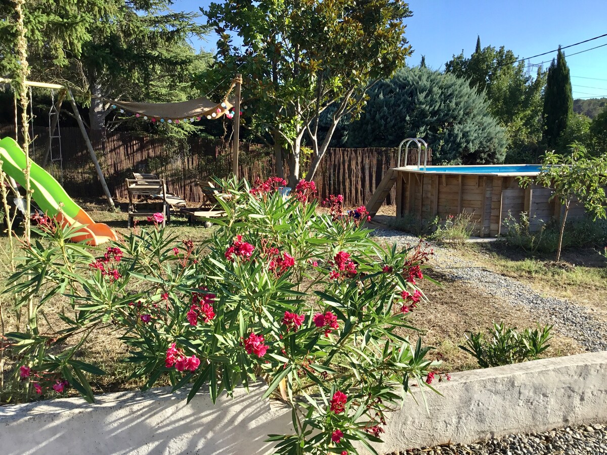 A private garden is depicted, featuring blooming flowers and a grassy area. A wooden above-ground pool is visible alongside a slide for children. Lounge chairs are positioned nearby, and a shaded hammock contributes to the outdoor leisure space.