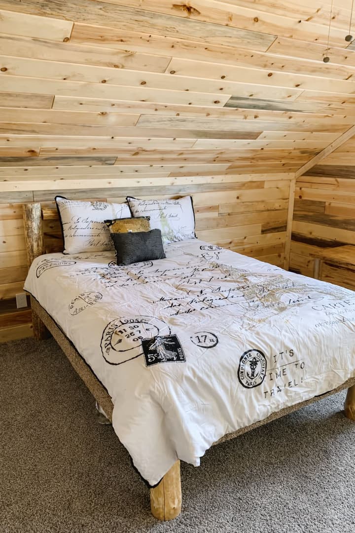 Dormitorio n.º 1 en la planta superior, con una acogedora cama queen de madera, paredes de madera cálida y luz natural, que ofrece un tranquilo refugio en Island Park.
