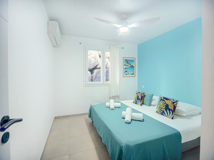 Habitación con aire acondicionado de estilo tropical, ideal para una estadía cómoda en Martinica. Ropa de cama de calidad, ventilación en el techo y ambiente suave para noches de descanso después de la playa o excursiones.