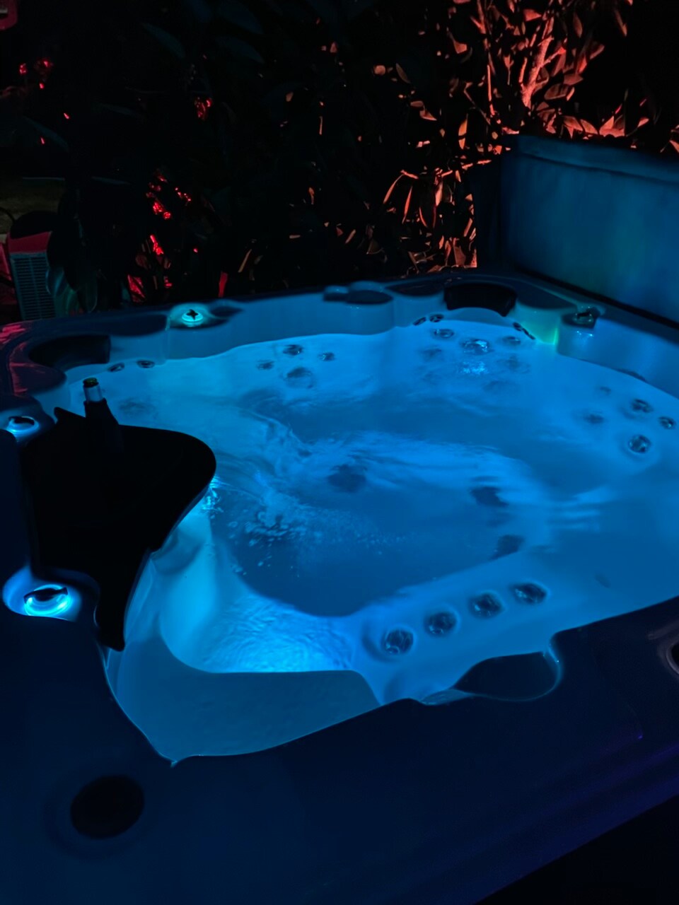 A hot tub glows softly under colorful lights, inviting relaxation. The water ripples gently, creating a soothing atmosphere. Surrounded by lush greenery, the setting offers a sense of privacy and tranquility, perfect for unwinding after a day of exploration.