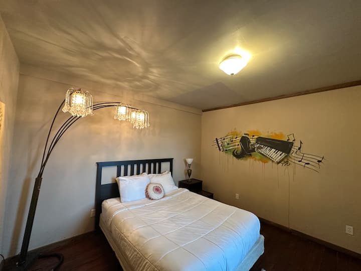 Elegant private master suite featuring a cozy queen size bed, crystal chandelier lighting, vintage décor, and artistic touches. Perfect for a relaxing Galveston getaway near cruise terminals, The Strand, dining, shopping, and beaches.