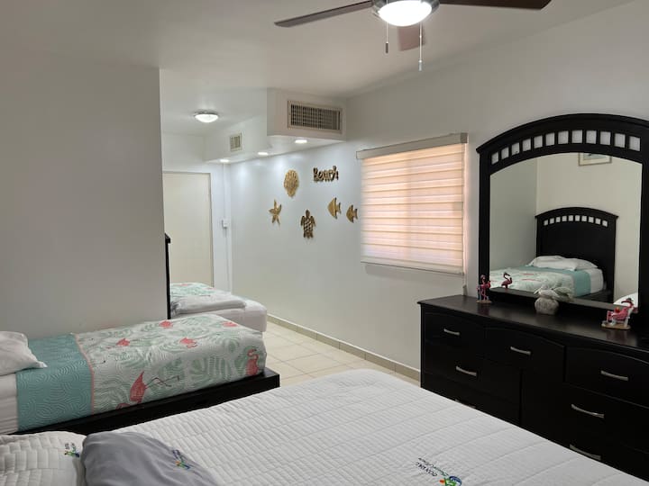 Recámara principal con 4 camas: 1 KS, 3 camas individuales. 1 TV de 50”. Equipada con AC tipo central y 1 minisplit de 1.5 toneladas (solo frío), 1 abanico de techo. Área para colgar y guardar ropa. 1 baño completo dentro de la recámara. 