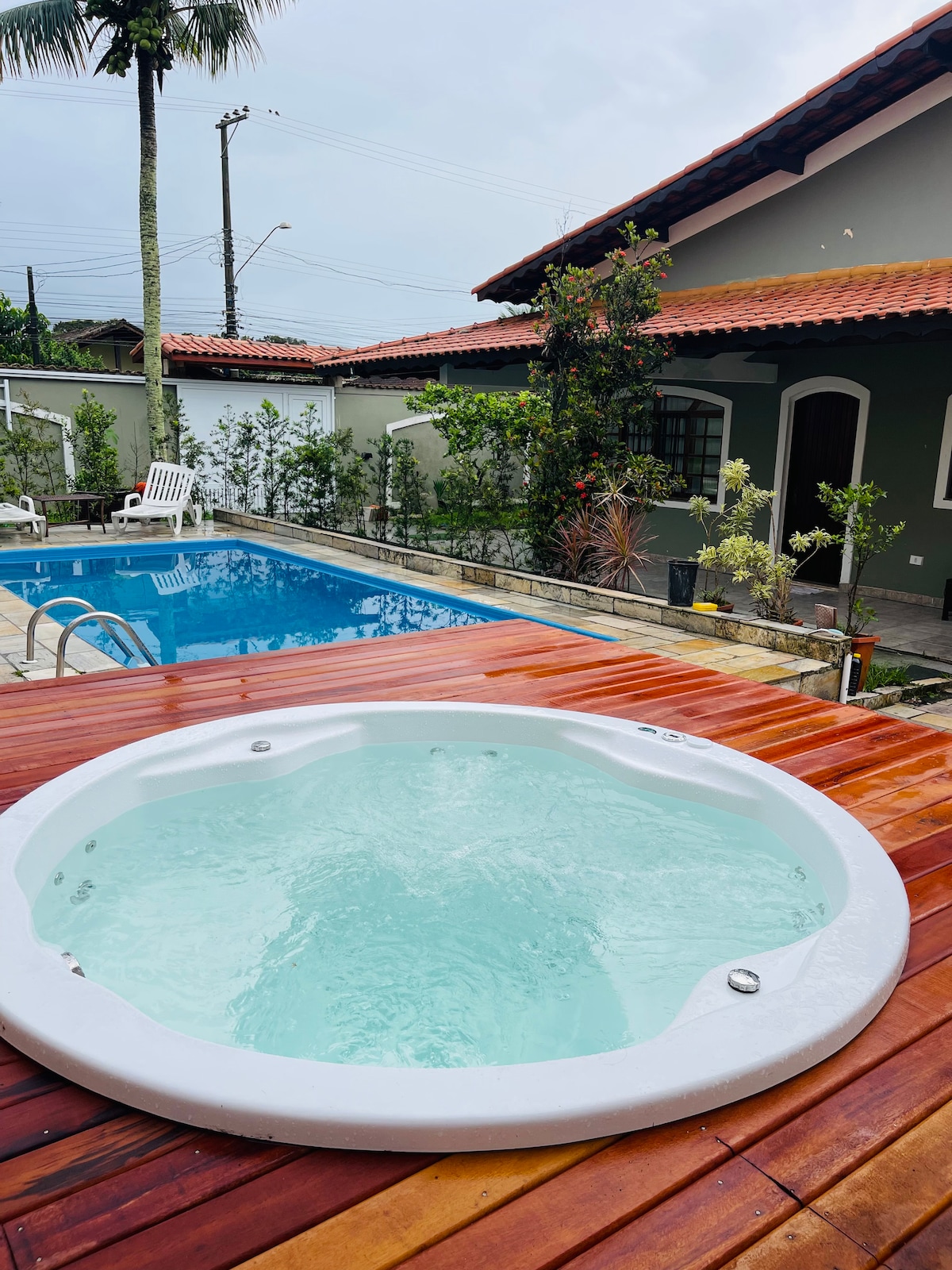 A private outdoor area features a hot tub on a wooden deck, with soothing water visible. Adjacent is a swimming pool surrounded by garden greenery, providing a refreshing atmosphere. The rustic building is partially visible in the background, showcasing charming architectural details.