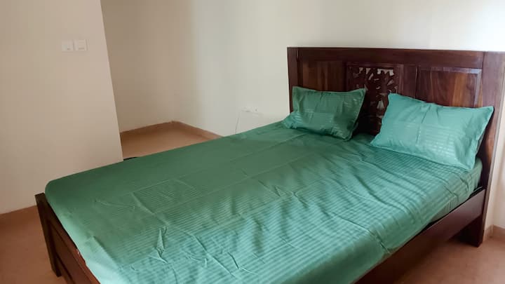 Wake up to birdsong in a serene bedroom with large windows overlooking lush greenery. Enjoy a restful sleep and relax in the attached bathroom with a walk-in shower. The gentle breeze and natural light create a peaceful retreat.