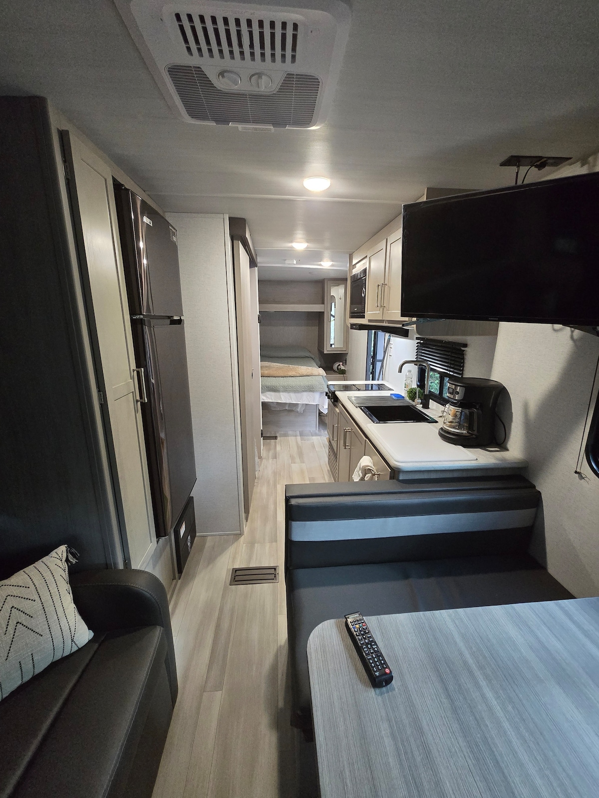 The interior of the trailer is visible, featuring a streamlined layout. A small kitchen area with appliances is to the right, while a dining space with a table and seating is present. A comfortable sofa and a doorway leading to the sleeping area are also seen.