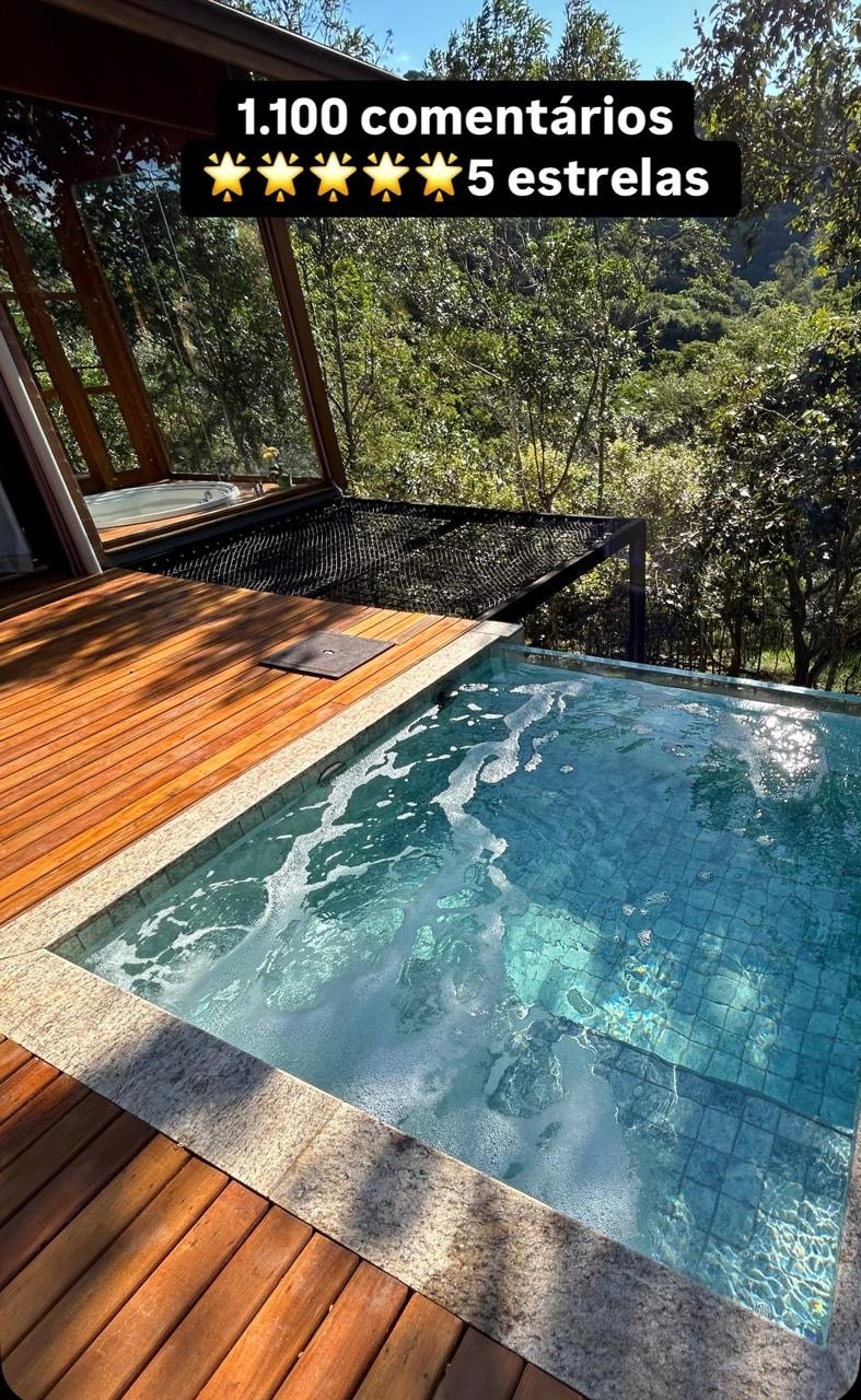 A glass-enclosed balcony features a sparkling jacuzzi surrounded by natural scenery. The wooden deck provides ample space for relaxation, complementing the luxurious touch of the bubbling water in the jacuzzi.