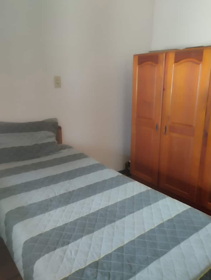 quarto individual com cama de solteiro 
guarda roupa em madeira 
tela mosquiteira na janela  com vista para a varanda
