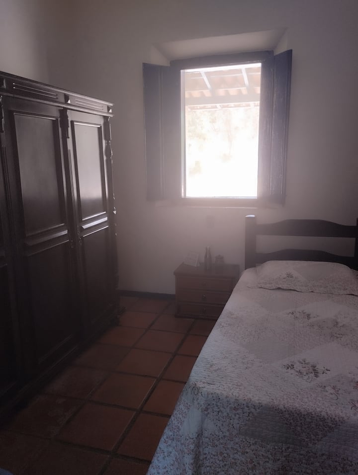 quarto individual com cama de solteiro 
mesa de cabeceira 
guarda roupa em madeira 
tela mosquiteira na janela com vista para a varanda