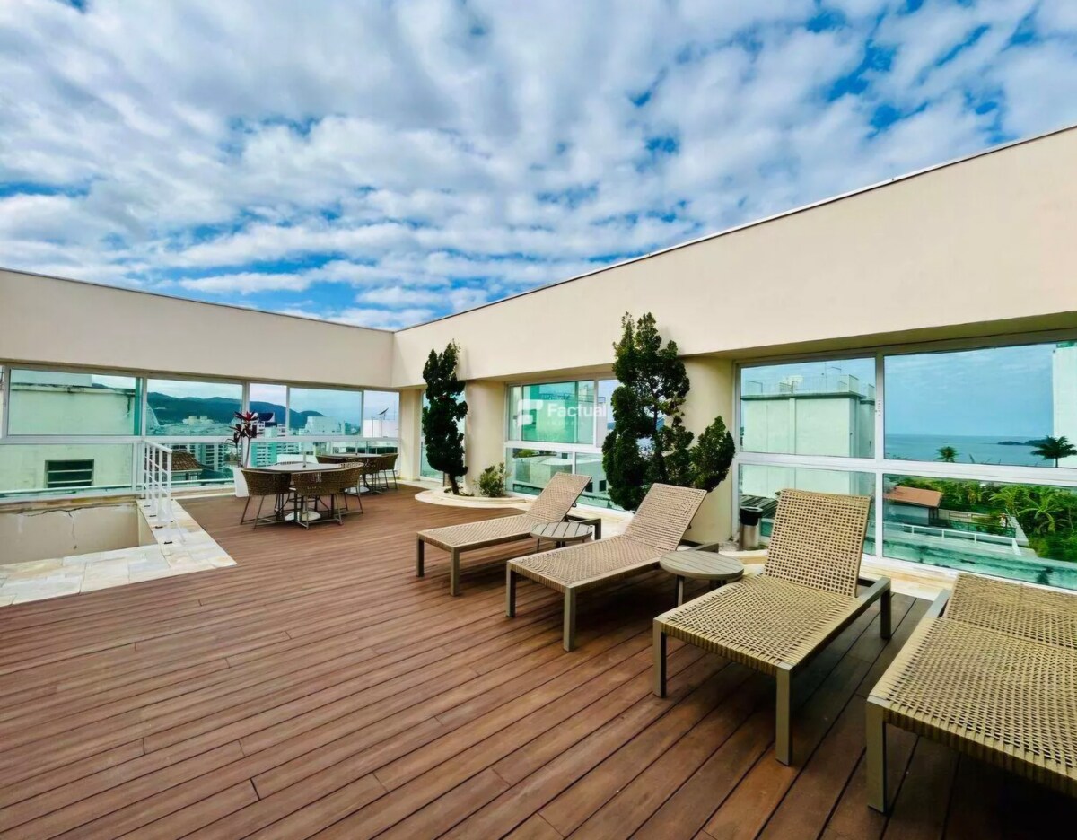A spacious rooftop terrace is depicted, featuring multiple lounge chairs arranged neatly on wooden decking. Large windows offer views of the surrounding area, while potted plants add a touch of greenery. The open space provides an inviting atmosphere for relaxation and enjoyment.