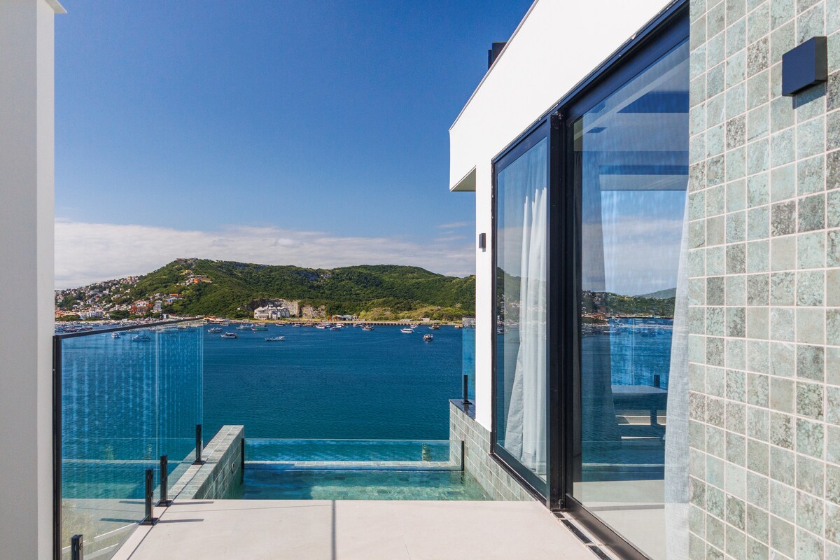 A stunning view of the ocean is captured from the terrace, framed by large glass doors and sleek, modern architecture. The infinity pool extends toward the water, creating a seamless connection with the landscape beyond.