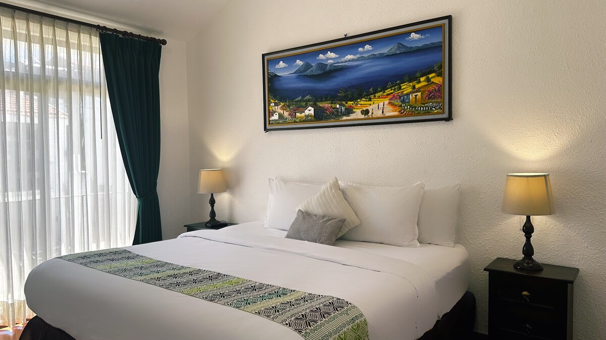 חדר שינה ראשי עם מיטת קינג סייז, טלוויזיה חכמה, אור טבעי ווילונות האפלה. נייר כסף מובא מציור של Panajachel ו - Lago de Atitlán שמביא מגע תרבותי ואותנטי לחלל.