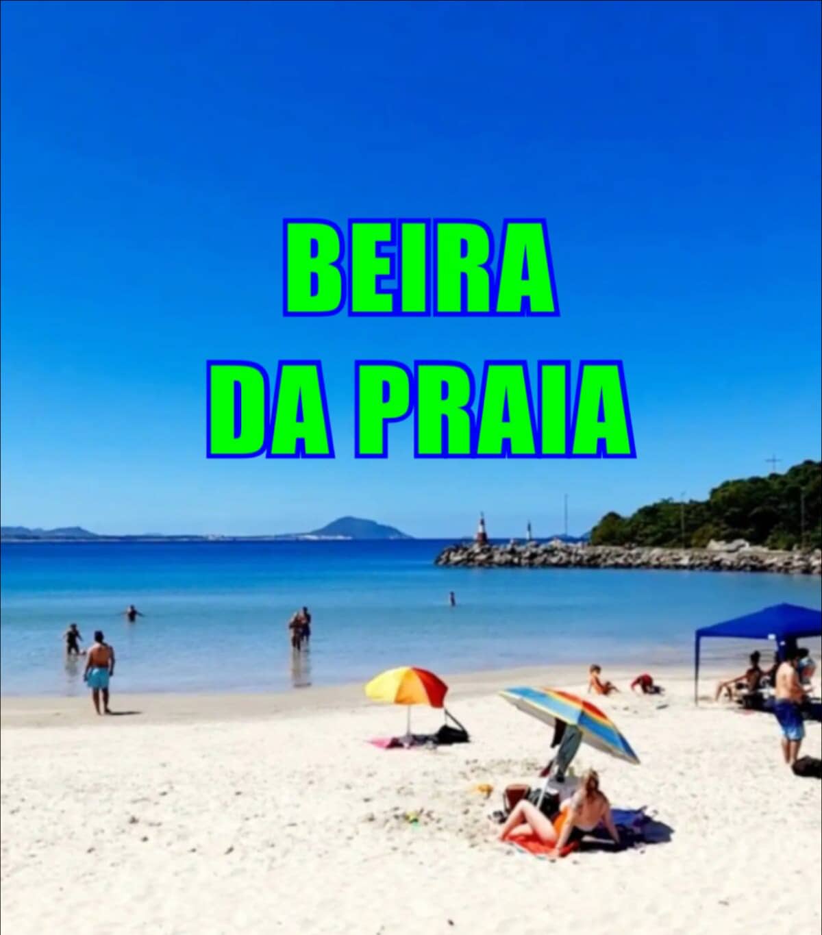 Sand stretches along the shoreline, where sunbathers relax under colorful umbrellas. The blue ocean sparkles under a clear sky, with distant hills framing the horizon. A lively atmosphere is created by people enjoying the beach, while a shaded area is provided by a tent.