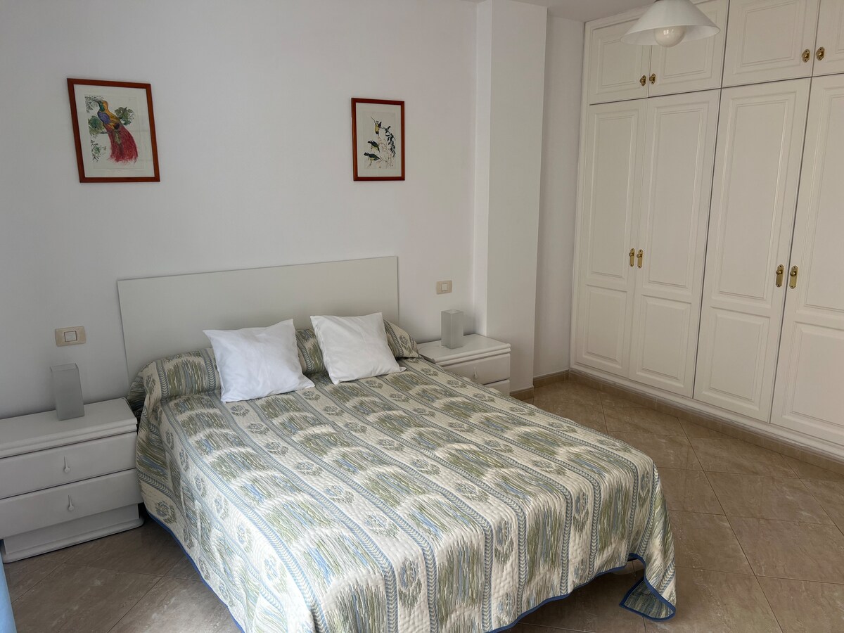A spacious bedroom features a large bed with decorative bedding and two pillows. Artwork adorns the walls, complemented by bedside tables and lamps. Ample closet space is available with white cabinetry, enhancing the overall light and airy atmosphere.