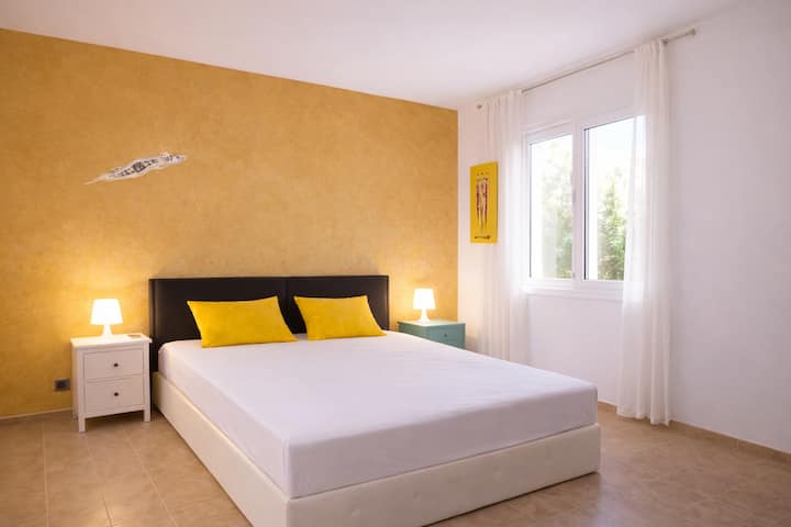 Habitación doble luminosa con una cama grande y cómoda, colores cálidos y un ambiente relajante. La ventana deja entrar mucha luz natural. Ideal para parejas o viajeros que buscan tranquilidad y comodidad después de un día en la playa.