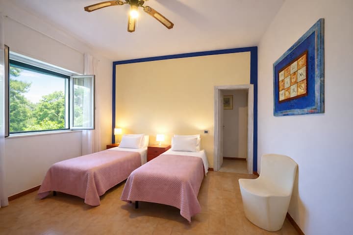Habitación doble luminosa con 2 camas individuales, colores cálidos y un ambiente relajante. La ventana deja entrar mucha luz natural. Ideal para parejas o viajeros que buscan tranquilidad y comodidad después de un día en la playa.
