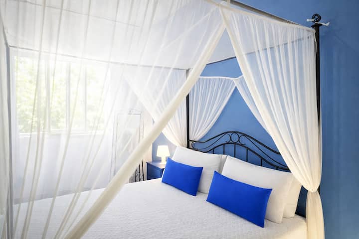 Habitación doble luminosa con una cama con dosel grande y cómoda, colores cálidos y un ambiente relajante. La ventana deja entrar mucha luz natural. Ideal para parejas o viajeros que buscan tranquilidad y comodidad después de un día en la playa.