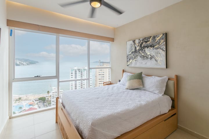 Recámara acogedora con cama queen e individual, iluminada por un gran ventanal que ofrece una vista agradable y un ambiente relajante.