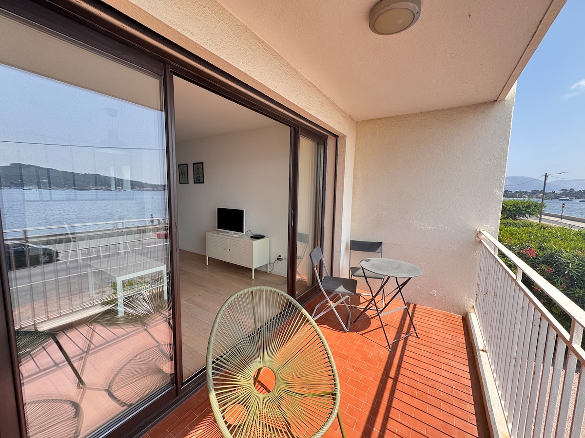 A balcony is featured with outdoor furniture, including a small round table and two chairs. The space offers views of the water, enhancing the connection to the surroundings. Large sliding glass doors lead into the living area, allowing natural light to fill the space.