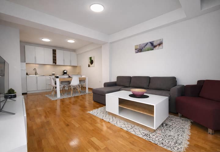 Просторна всекидневна с отворен план, удобни дивани, телевизор, трапезна маса и напълно оборудвана кухня. Чисто, уютно и идеално за пътуващи.