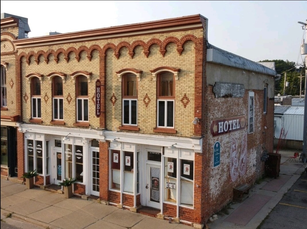 An updated two-story hotel building features a blend of classic brick architecture with ornate detailing. Large windows sit above the entrance, which is framed by flower boxes. The hotel's name is displayed prominently, enhancing its welcoming presence within the downtown area.
