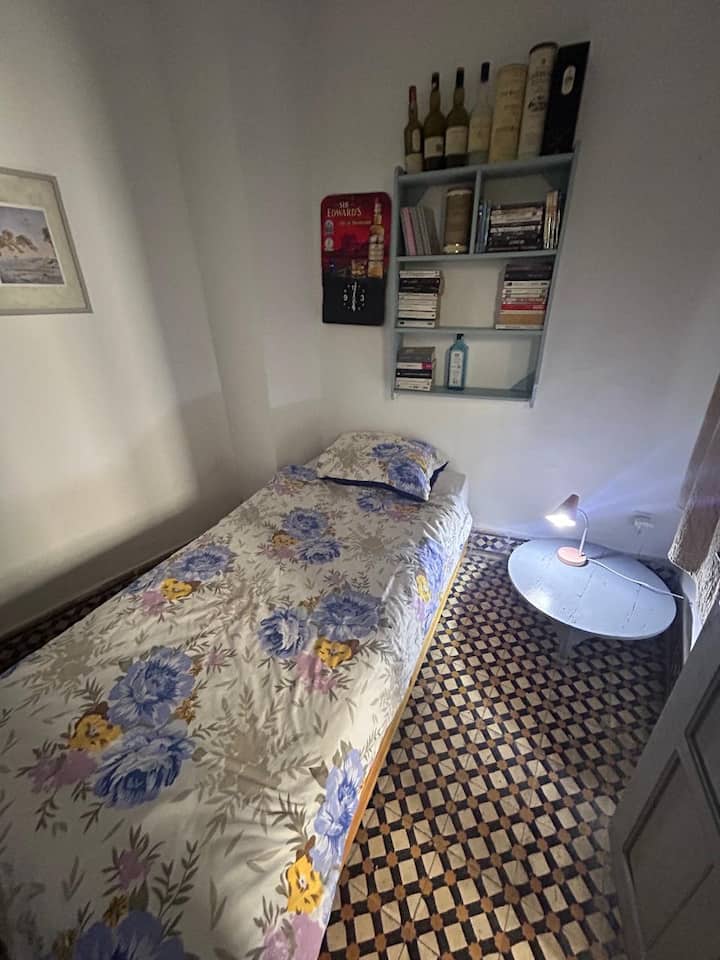 Chambre simple cosy avec lit confortable, idéale pour une personne. Décoration sobre, étagères avec livres et ambiance calme. Parfaite pour se reposer après une journée ou pour un séjour tranquille.
