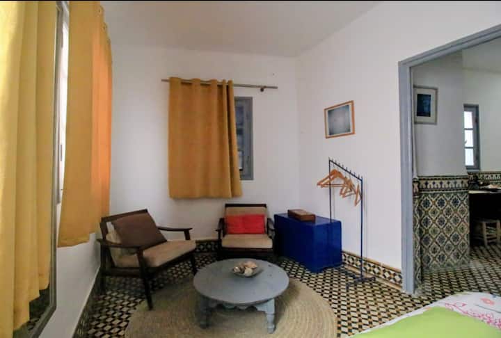 Chambre double chaleureuse avec lit double, coin salon avec fauteuils et table basse, carreaux de ciment traditionnels et grands rideaux dorés. Une suite cosy pour un séjour tout en confort.