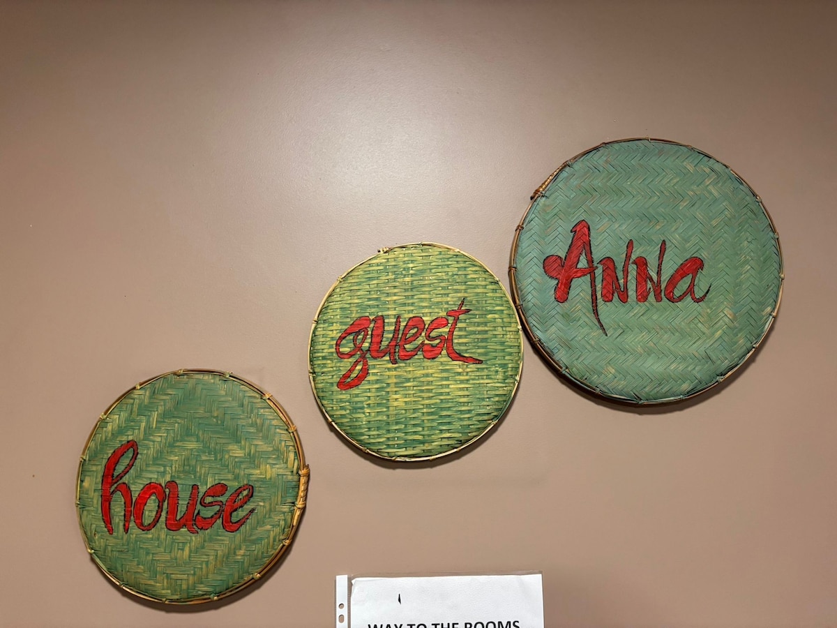 Three decorative woven circular wall hangings are arranged on a neutral-toned wall. Each piece features a different word: 'house' in red, 'guest' in green, and 'Awhile' in red. The textured backgrounds enhance the artisanal visual appeal.